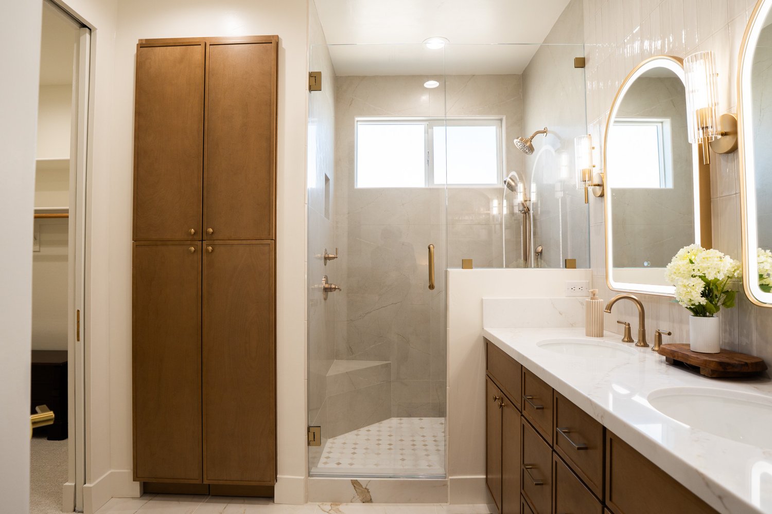 Primary bathroom after — glass walk-in marble shower, double vanity, brass fixtures